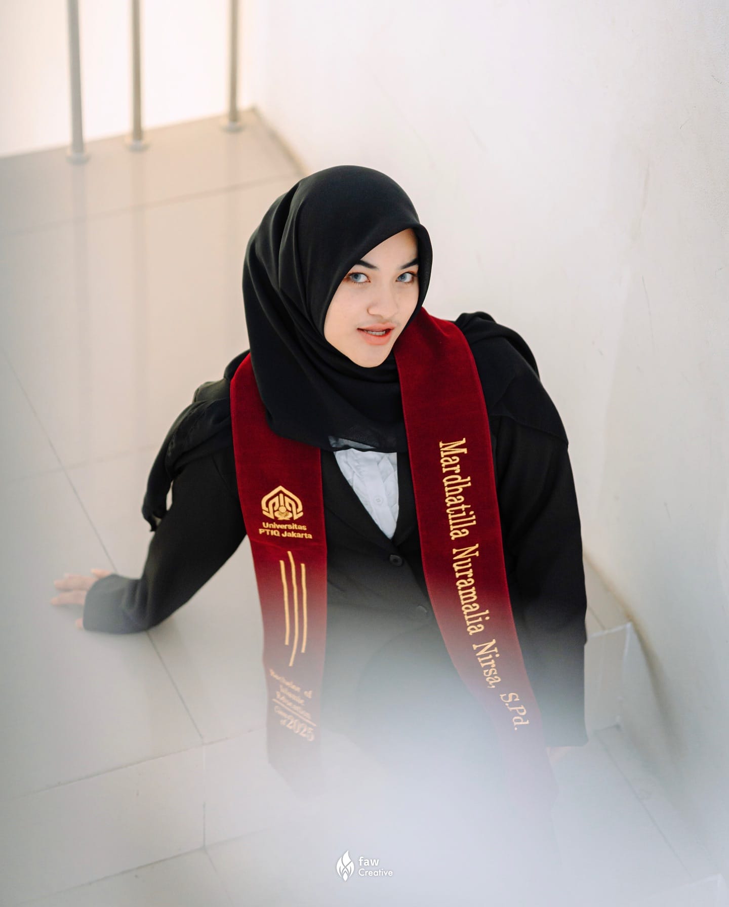 Wisudawati PTIQ Jakarta menoleh ke kamera dari tangga, selempang maroon bertuliskan namanya